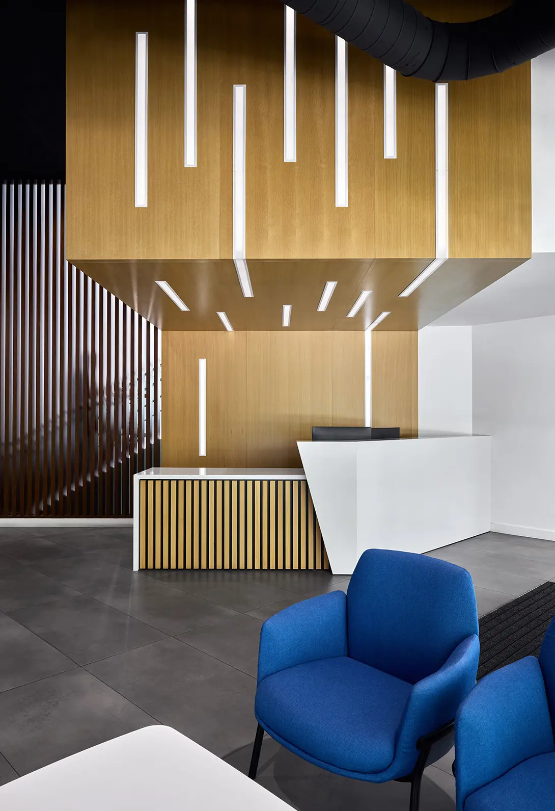 Modern office reception with wood panel design, white desk, blue chairs, and ambient lighting.